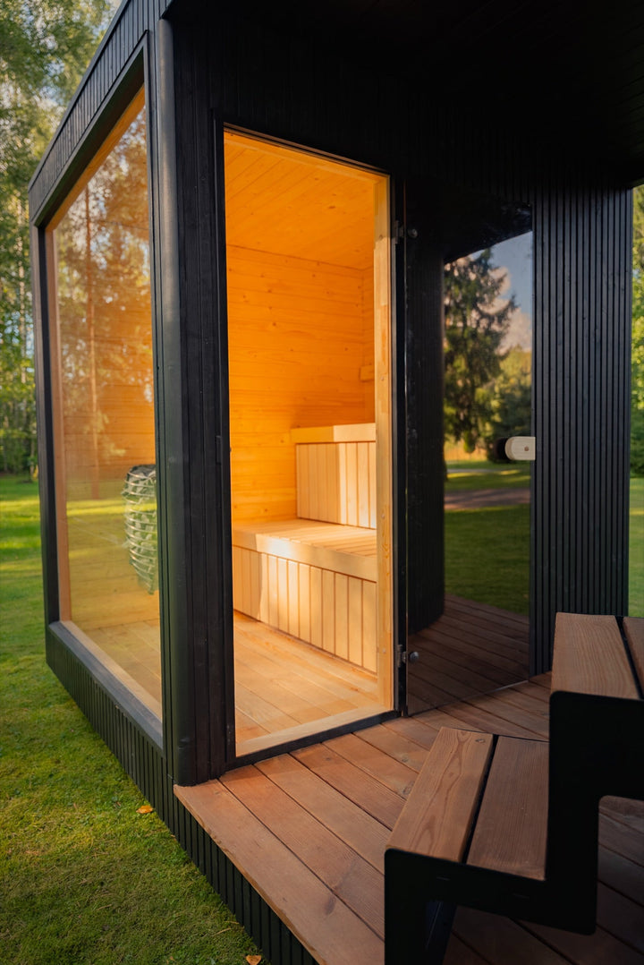 Eingang der Gartensauna KOTI L – offene Glastür, helle Bänke und Holzterrasse mit Sitzbank