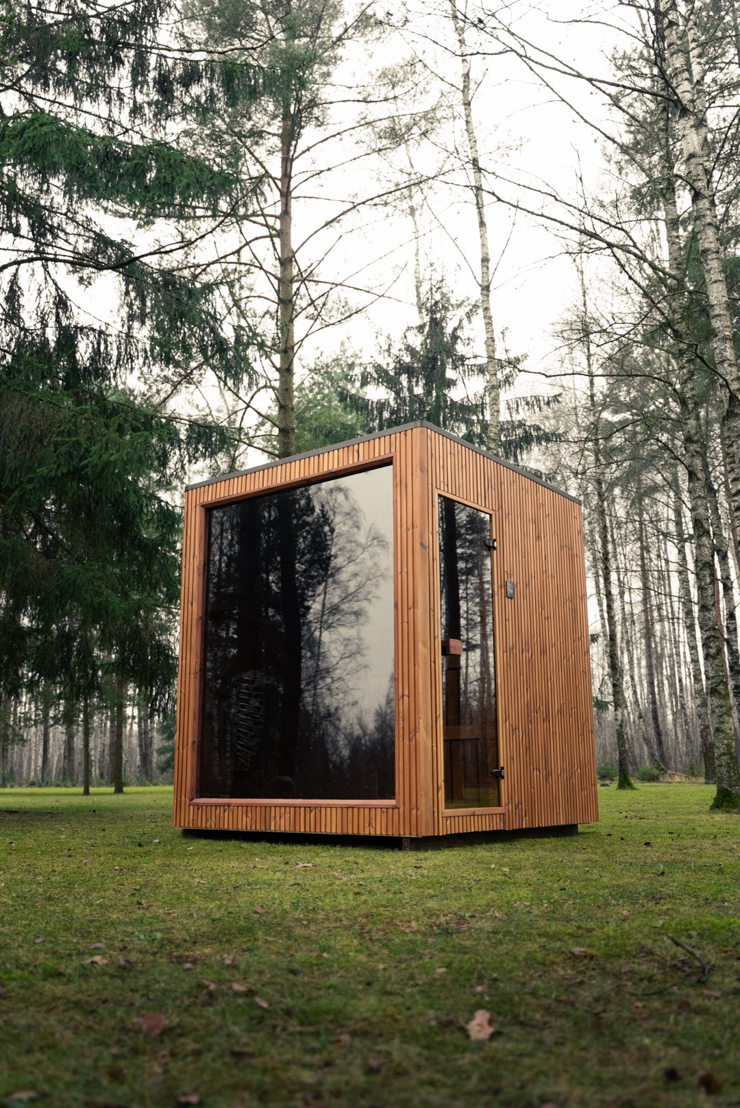 Sauna ogrodowa VALO S z dołu – przeszklona ściana frontowa i szklane drzwi w brązowej drewnianej elewacji