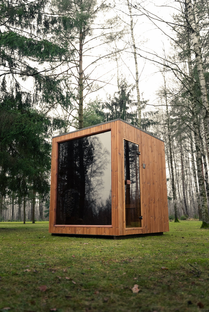 Sauna ogrodowa VALO S z dołu – przeszklona ściana frontowa i szklane drzwi w brązowej drewnianej elewacji